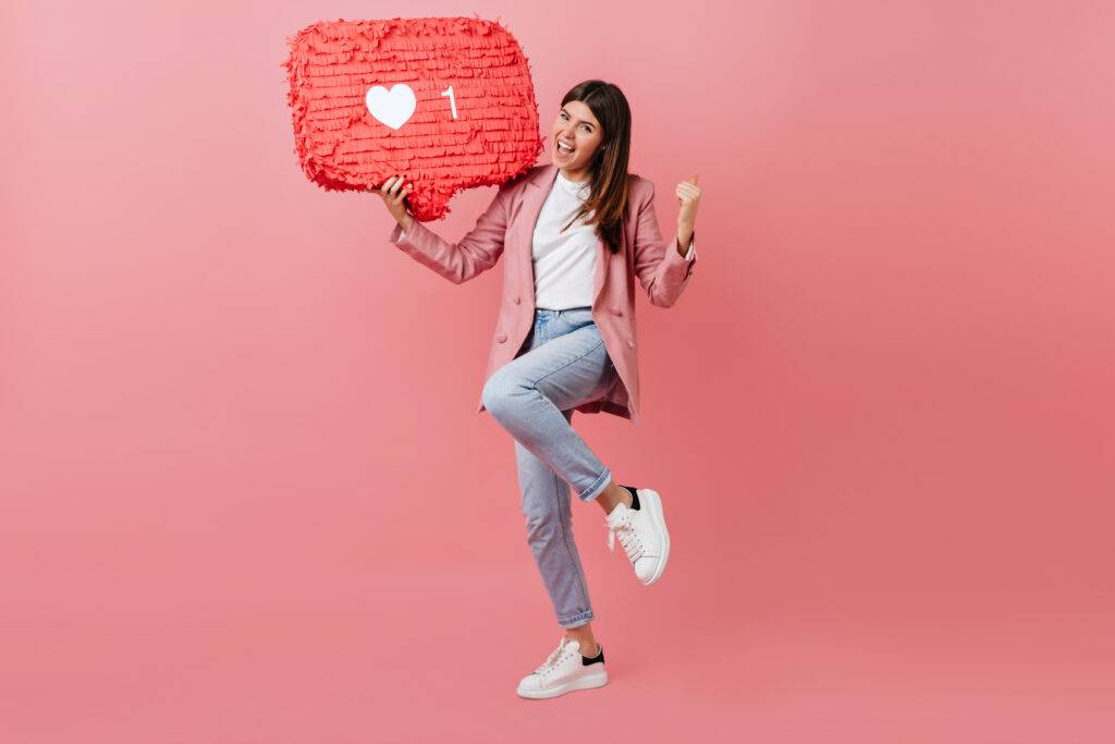 girl enjoying social network feedback studio shot of young woman dancing with like icon on pink background scaled